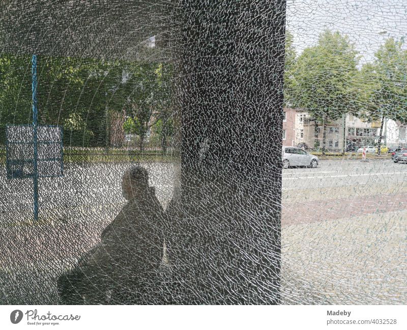 Sitzender Mann hinter der zersplitterten Scheibe einer Haltestelle vor der Kunsthalle Bielefeld im Teutoburger Wald in Ostwestfalen-Lippe Bushaktestelle