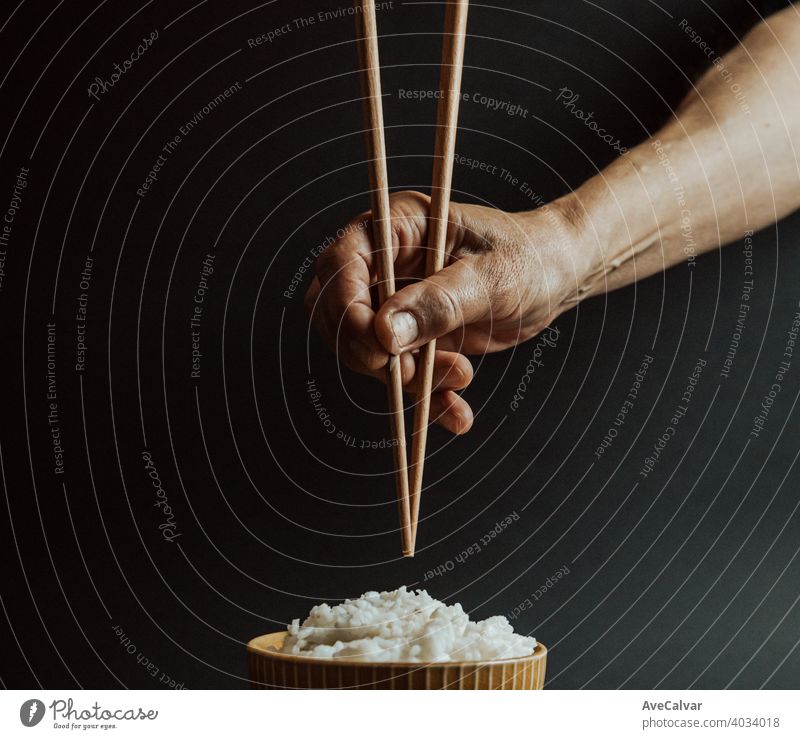 Minimalistische alte Hände greifen japanische Essstäbchen über eine Schüssel Reis Konzept Schuss auf filmische Töne über einen schwarzen Hintergrund Japanisch