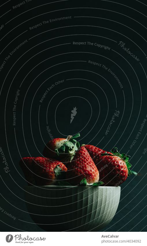 Eine minimale Aufnahme eines Erdbeerstraußes in einer Schüssel vor einem dunklen Hintergrund mit Kopierraum Erdbeeren farbenfroh Minimalismus Tapete horizontal