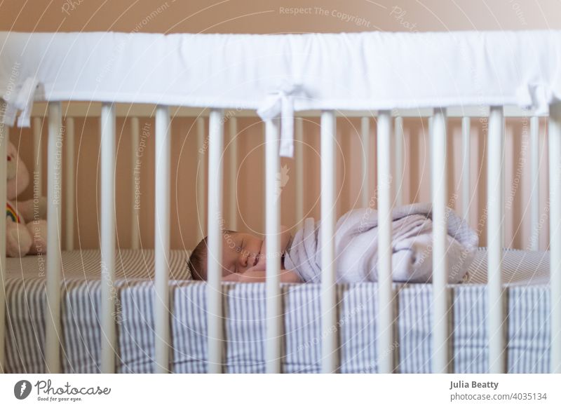 Neugeborenes Baby in Musselin gewickelt swaddle Decke in Krippe; Pfirsich Wände mit weißen und grauen Bettwäsche im Kinderzimmer Mittagsschlaf schlafen