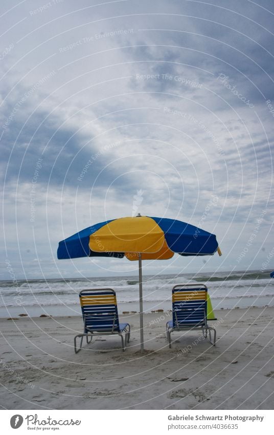 Einsame Liegestühle am Meer Liegestuhl Strand leer Wellen Wellengang Gischt Sand Sandstrand Streifen gestreift blau gelb Sonnenschirm Seetang Wolken