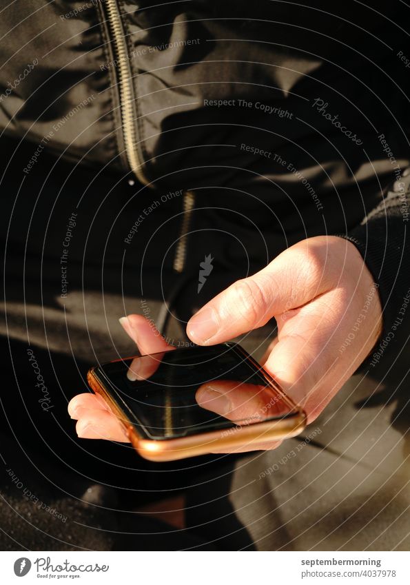 Handy in einer Hand Handy bronzefarben Männerhand hell schwarze Jacke schwarze Hose Fingerspiegelung im Handy