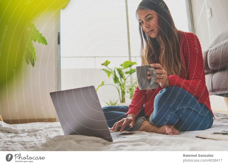 Eine Frau, die Tee trinkt, auf dem Boden einer Wohnung sitzt und sich Notizen macht, hat einen Laptop vor sich aufgeklappt. Home-Office-Konzept. Bietet Kaffee an. Konzept kreative Arbeit zu Hause. Selektiver Fokus.