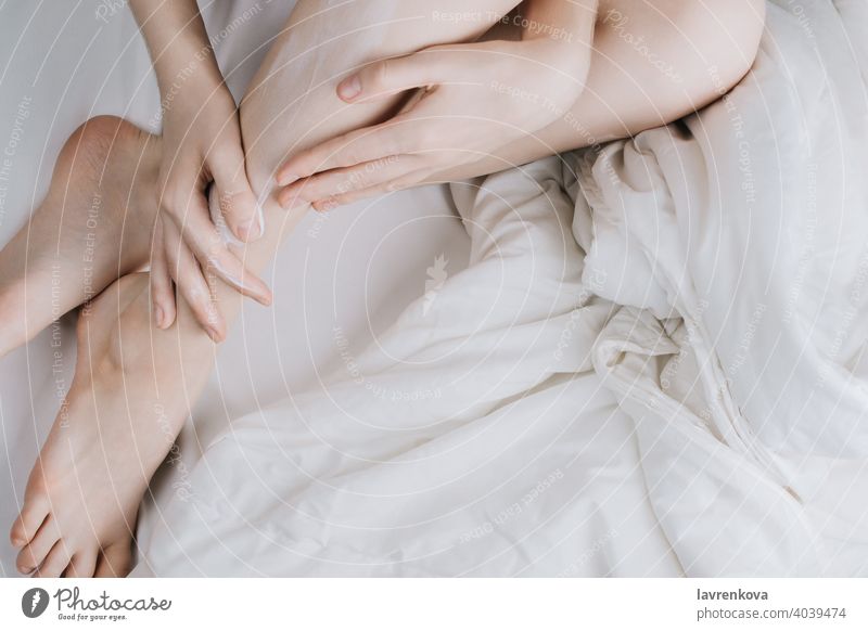 Flatlay von Frau reiben Creme in ihre Beine im Bett Schönheit Aftershave Körper Hautpflege Kaukasier Sahne Finger Fuß sanft Mädchen Erdöl Person Reibung weiß