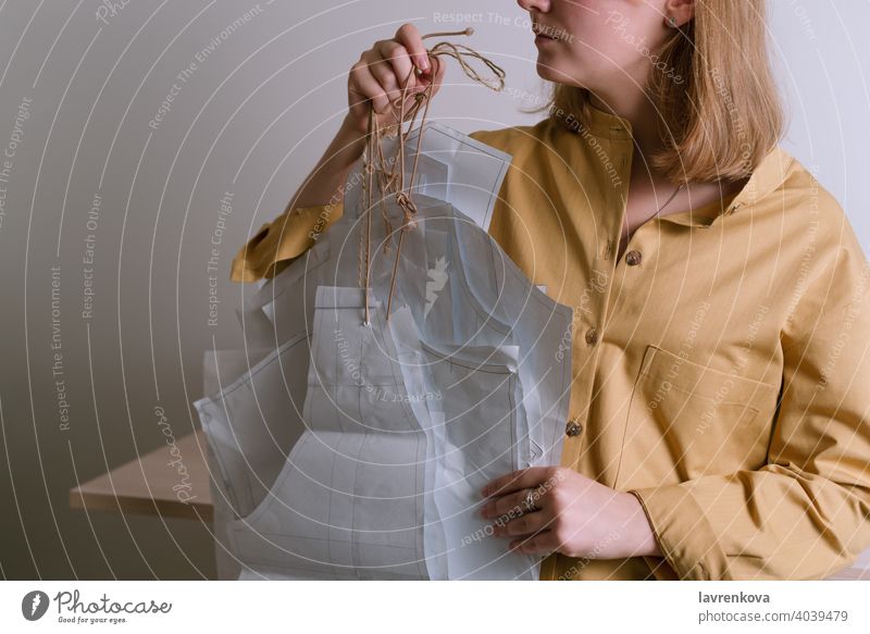 Frau in gelbem Hemd hält Papierkleidmuster in ihrer Werkstatt Schneider Handwerk Damenschneiderin Mode Muster Kleid Kleidungsmuster Bekleidung Beruf