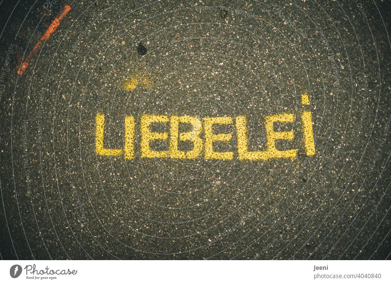 Ein Weg mit Straßenmalerei oder Graffiti mit dem Wort "LIEBELEI" | kleiner orange farbiger Streifen oben links | Text auf einfarbigem neutralen Hintergrund