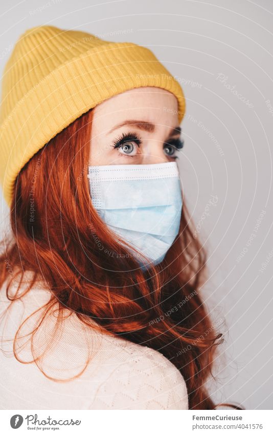 Rothaarige junge Frau mit gelber Hipster Beanie Mütze trägt eine medizinische Maske - Portrait mit Profil Maskenpflicht Beaniemütze beanie rothaarig lange Haare