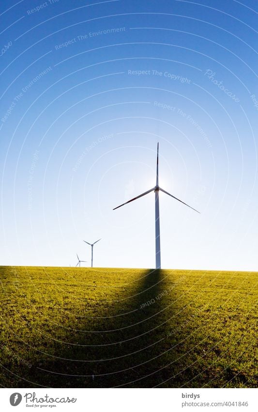 Windkraftanlagen auf dem Feld im Gegenlicht vor blauem Himmel. Schattenwurf von Mast, Sonne hinter dem Generator regenerative energie Erneuerbare Energie