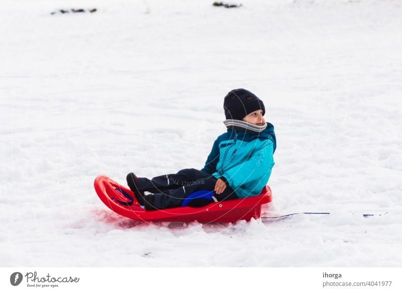 Junge mit rotem Schlitten im Schnee Winter aktiv Kind Kindheit kalt Spaß lustig Fröhlichkeit Glück Hut Feiertag Kinder gestrickt Freizeit wenig Berge u. Gebirge