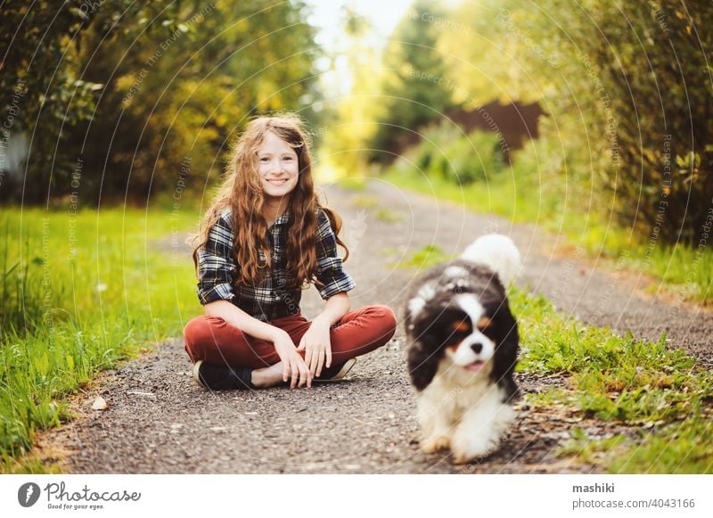 glückliches Kind Mädchen zu Fuß mit ihrem Cavalier King Charles Spaniel Hund auf Sommer Landstraße. Training ihr Welpe und Spaß haben. Tier Haustier Natur