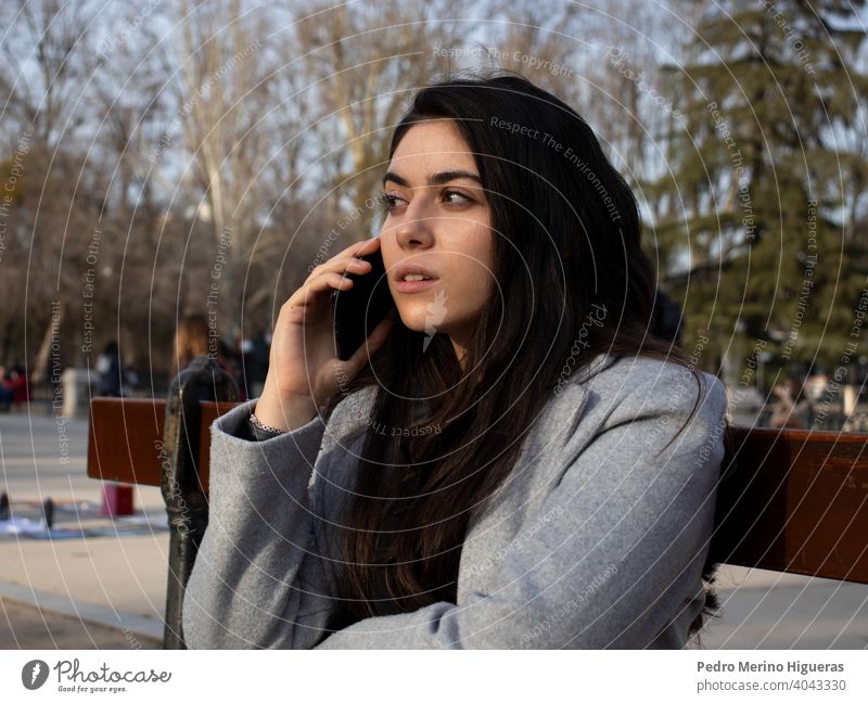 Frau sitzt auf einer Bank und spricht mit ihrem Handy in einem Park. Person Teilnahme an Smartphone laufen sprechend Gespräch Telefon Ärger Nachrichten
