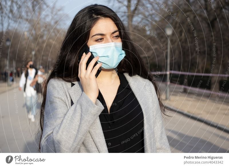 Frau mit Gesichtsmaske im Gespräch mit ihrem Handy in einem Park. Person Erwachsener Verschmutzung Telefon Air Pflege Staubwischen Pandemie Kaukasier Seuche