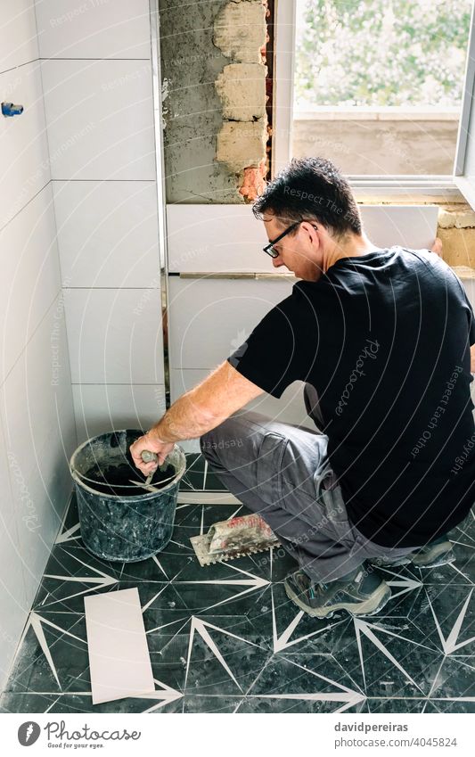 Maurer nimmt Zement aus dem Eimer, um Badezimmerfliesen zu verlegen Reform Fliesen u. Kacheln Wand Beton Spachtel diy Maurerhandwerk Arbeiter Kaukasier Mann