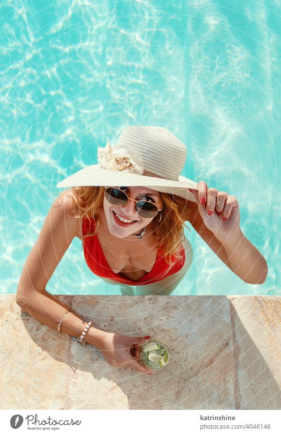 Junge Frau in rotem Badeanzug und Strohhut mit tropischen Cocktaileinlagen Hut Mojito Pool Wasser Sommer jung Kaukasier Schwimmbad Mode blau türkis allein Glück