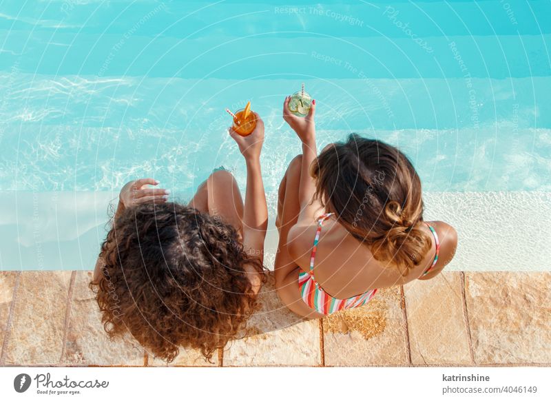 Zwei junge Frauen in Badeanzügen entspannen und trinken tropische Cocktails Badeanzug Mojito Pool Wasser Sommer Freunde Party multiethnisch Zusammensein