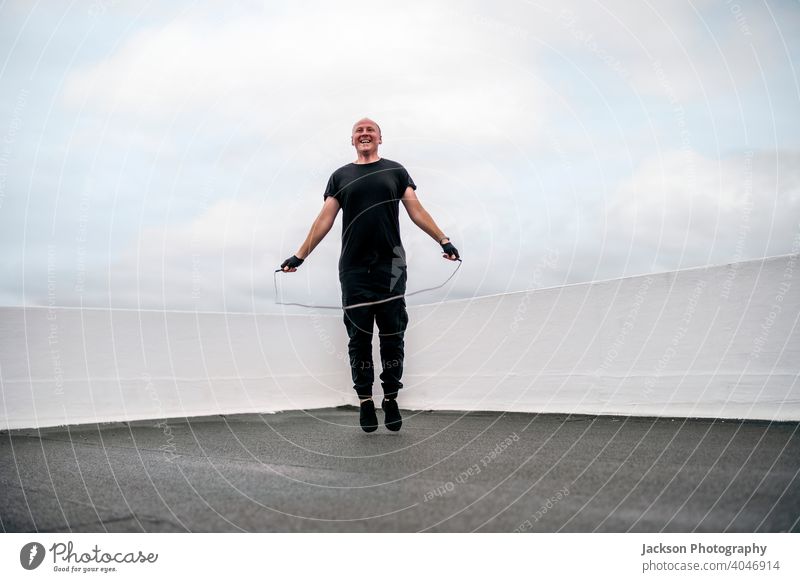 Ein Mann, der während der Abriegelung auf dem Dach mit einem Springseil trainiert Sperrung Sport Dachterrasse Pandemie Seil Hüpfseil Herz Ausdauer seilhüpfen