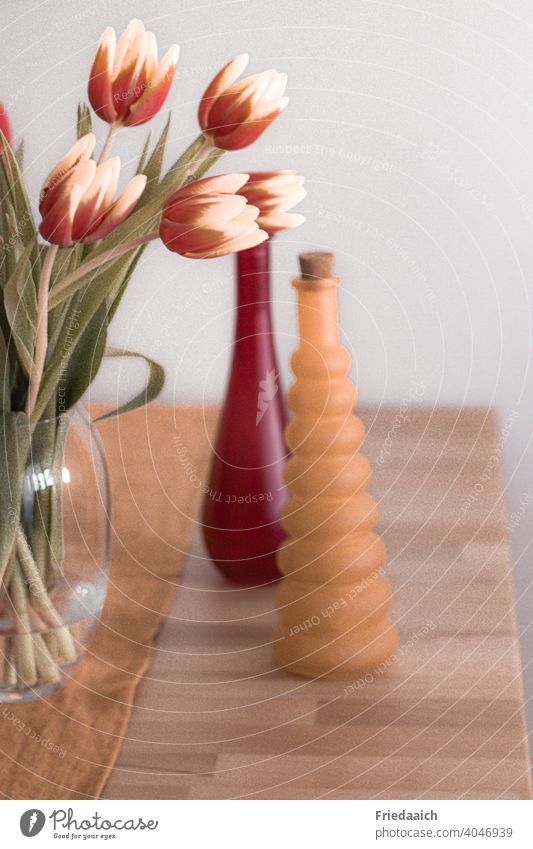 Glasvase mit Tulpen und bunte Zierflaschen auf dem Holztisch Stillleben Vase mit Blumen Frühling Blumenstrauß Dekoration zuhause gemütlich farbenfroh