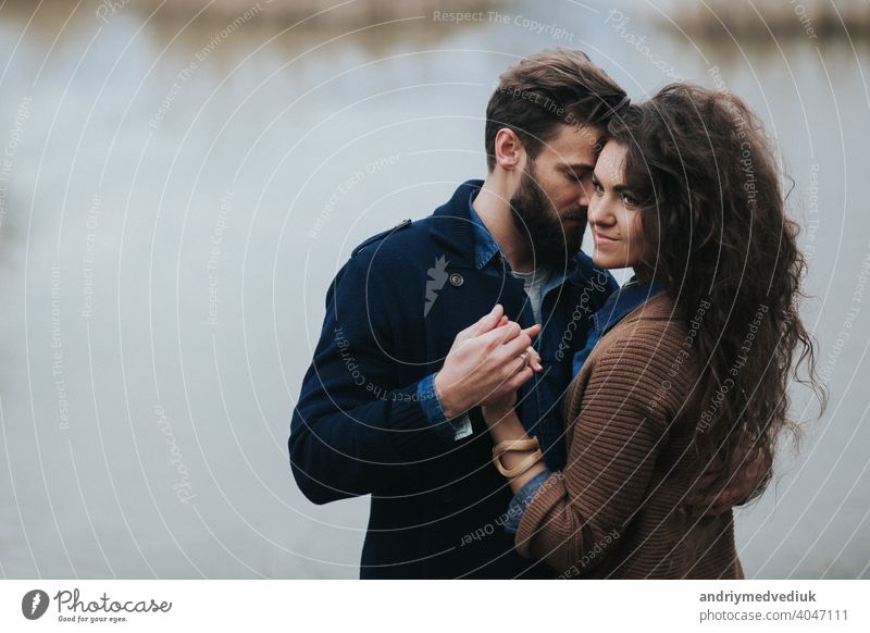 Glückliche Liebende in der Nähe des Sees. Junges Paar umarmt sich am Herbsttag im Freien. Ein bärtiger Mann und lockige Frau in der Liebe. Valentinstag. Konzept der Liebe und Familie.
