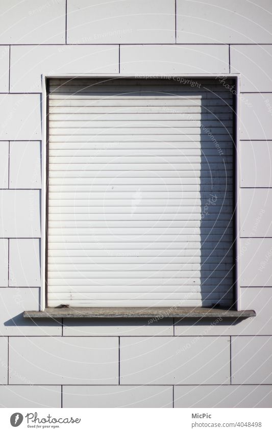 Weiße Hausfassade, ein Fenster mit geschlossenen weißen Rollladen Fassade weißer Hintergrund Lockdown Fensterladen Schattenwurf klar leer Leerstand