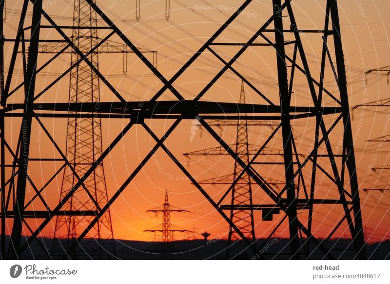 Strommasten vor Abendhimmel, durch einen Strommasten im Vordergrund aufgenommen, angeschnitten, orange-schwarz Detailaufnahme Hochspannungsleitung Abendsonne