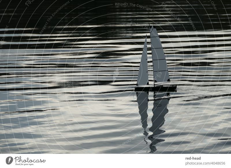 kleines Segelboot, Modellboot von der Seite, Spiegelung der Segel im Wasser, horizontale Linien durch Lichtwellen Wasseroberfläche Wasserspiegelung