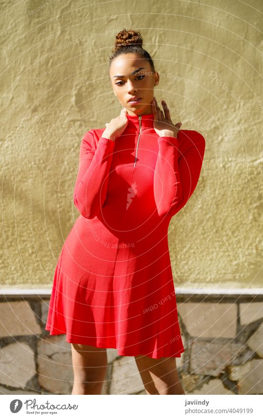 Junge schwarze Frau in rotem Kleid mit ernstem Gesichtsausdruck im städtischen Hintergrund. Schleife Frisur Behaarung Model Schönheit hübsch Porträt Mädchen