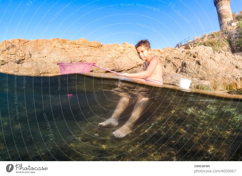 Kleiner Junge beim Fischen auf dem Meer mit einem Fischernetz allein Strand Felsblöcke fangend Kaukasier Kind Küste Rippenrohr niedlich Dänemark Genuss