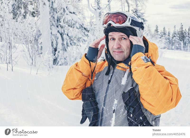 Kaukasischer Mann Snowboarder in weißen Helm und Latzhose auf Hintergrund verschneiten Wald. Winter aktiv Ruhe. Urlaub in den Bergen. Gesunder Lebensstil