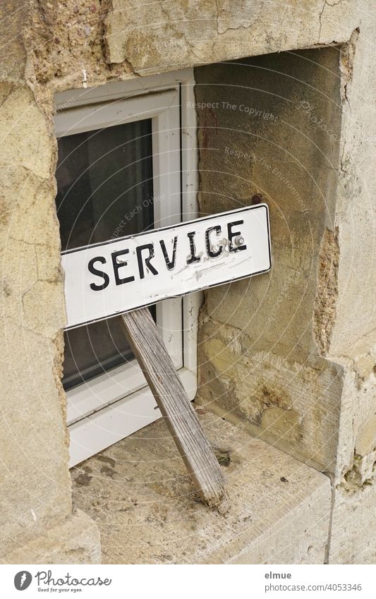 Ein eher marodes Schild mit der Aufschrift "SERVICE" lehnt vor einem kleinen Fenster eines langsam zerfallenden Hauses / Kundendienst Service Kundenservice