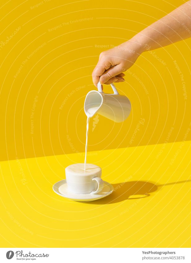 Milch in eine Tasse gießen, auf gelbem Hintergrund. Milch Überlauf aus einer Tasse Überfluss Getränk Frühstück hell Kalzium Karaffe farbig farbenfroh Farben