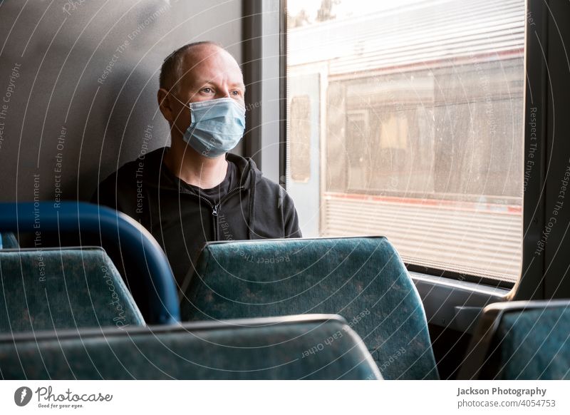 Ein Mann mit chirurgischer Maske schaut durch das Fenster in einem Zug Mundschutz Pandemie Blick ernst traurig Textfreiraum öffentlicher Verkehr COVID19