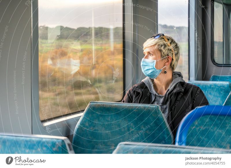 Frau mit chirurgischer Maske schaut durch das Fenster in einem Zug Mundschutz Pandemie Blick ernst traurig Textfreiraum öffentlicher Verkehr COVID19 Kaukasier