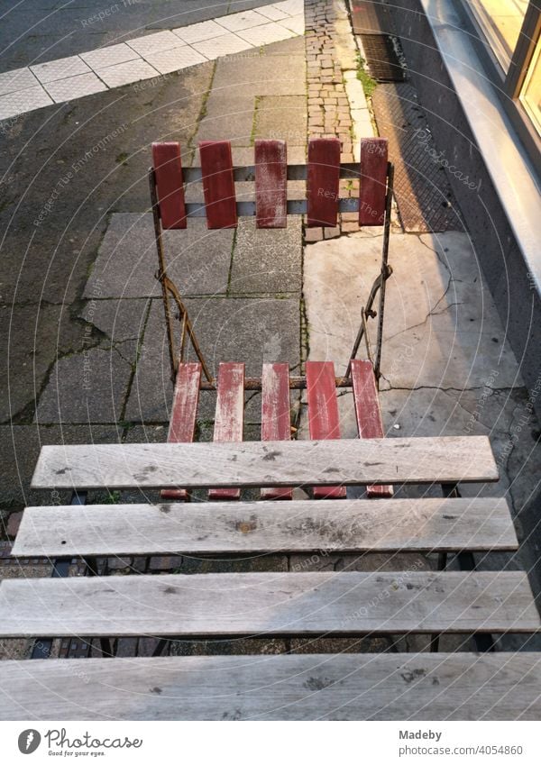 Bistrotisch mit Bistrostuhl auf wild zusammengewürfeltem Straßenpflaster bei Kunstlicht am Abend vor einem Schaufenster im Nordend von Frankfurt am Main in Hessen