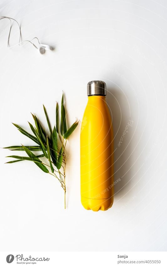 Eine gelbe Wasserflasche und ein Zweig Bambus auf einem isolierten weißen Hintergrund Wiederverwendbar Kopfhörer Fitness Flasche ökologisch Konzept Thermo Stahl