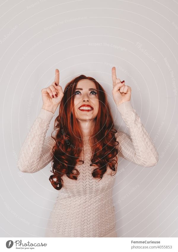 Frau mit langen roten lockigen Haaren schaut nach oben und zeigt auch mit beiden Händen und Zeigefingern nach oben zeigen hinweisen deuten Hinweis
