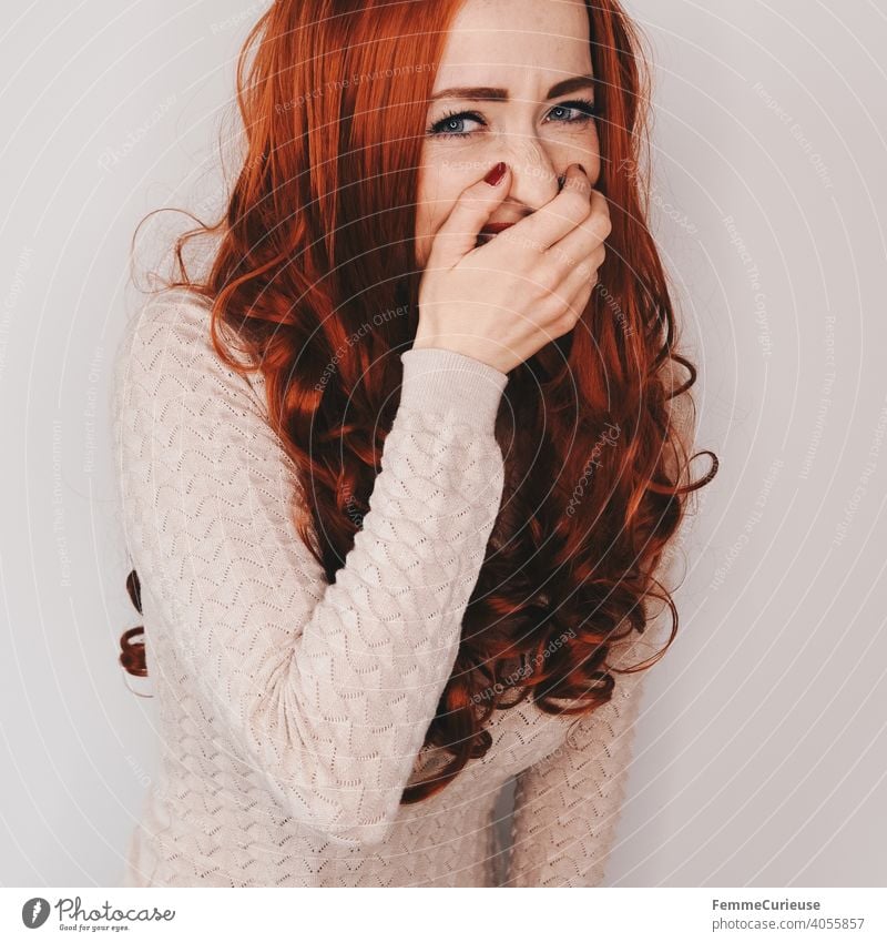 Frau mit langen roten lockigen Haaren lacht in Kamera schauend und hält sich dabei eine Hand vor den Mund Haare & Frisuren lange Haare rote Haare lockiges haar