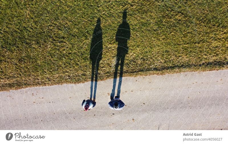Luftaufnahme mit einer Drohne von zwei Personen mit einem langen Schatten luftaufnahme drohnenfoto menschen personen mann frau paar straße wiese feld schatten