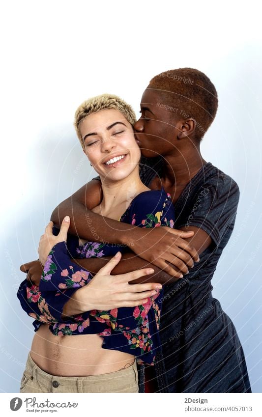 Fröhliche Damen, die sich küssen und umarmen, von verschiedenen Rassen, gekleidet in Freizeitkleidung. umarmend Küssen Paar Ethnizität Freundschaft