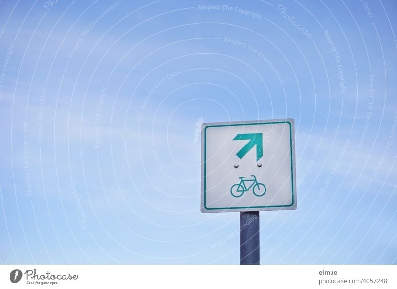 Ein quadratisches Schild vor blauem Himmel zeigt ein Fahrrad und einen Pfeil nach rechts oben / Piktogramm / Orientierung Radweg Radfahren HInweisschild