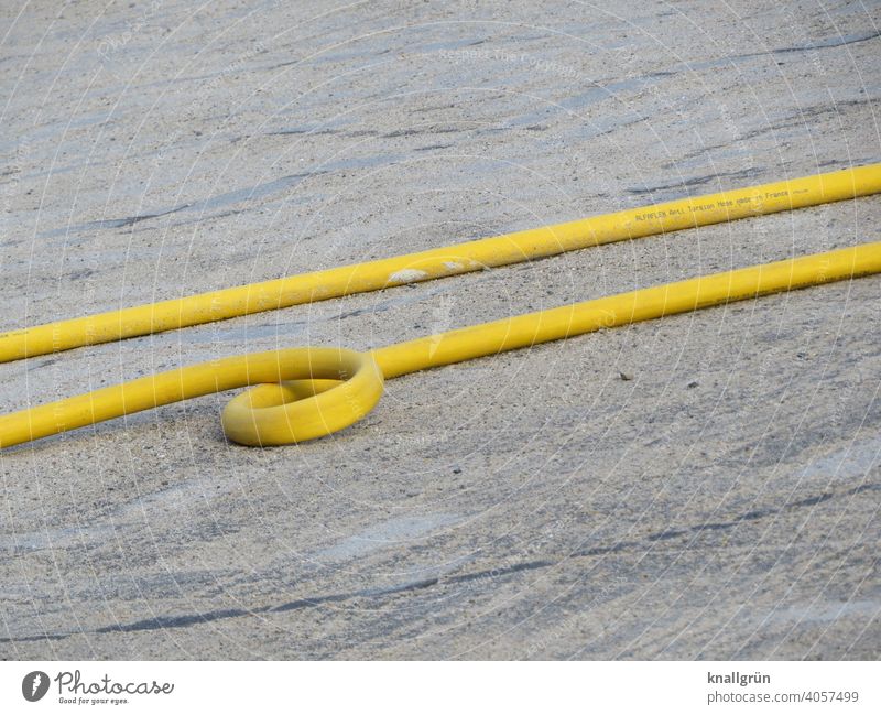 Gelber Wasserschlauch mit Looping Baustelle gelb Schlinge looping Schlauch Gartenschlauch Außenaufnahme Boden liegen nebeneinander parallel zwei rund grau