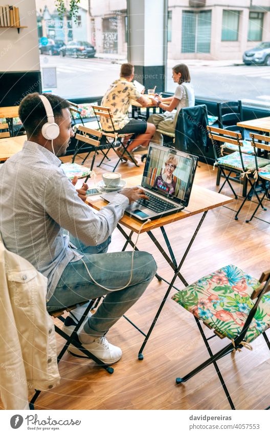 Mann spricht per Videoanruf mit seiner Mutter sprechend Laptop Kaffeehaus Internet Kopfhörer Bildschirm Videokonferenz männlich Café Tisch Familie