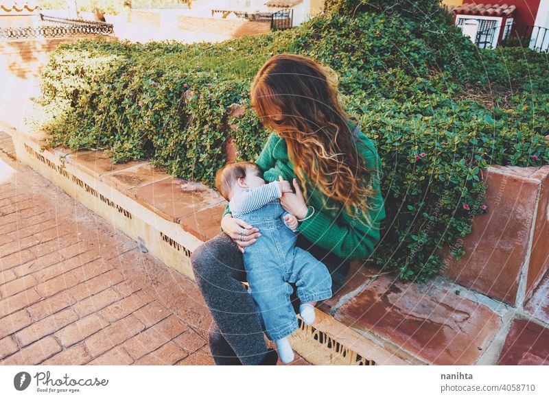 Junge Frau stillt ihr Baby im Freien an einem sonnigen Tag jung Mutter Mama Familie Stillen grün Feiertage Freizeit Gesundheit blond Pflege Kindheit