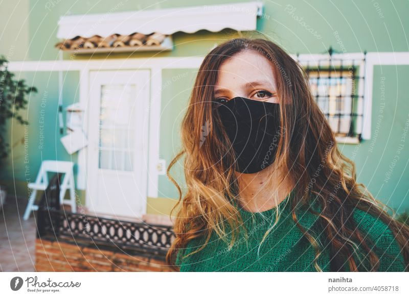 Junge Frau mit schwarzer Gesichtsmaske vor einer grünen Stadtmauer Coronavirus Mundschutz Kopfschuss lässig urban anhaben Leben wirklich echte Menschen