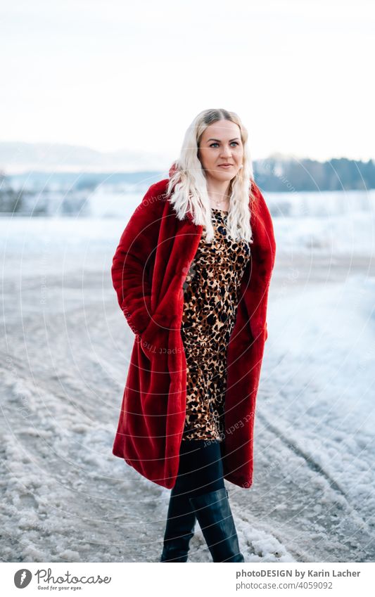 junge Frau 30 Jahre im Schnee mit rotem Mantel und Leoparden Kleid blonde Haare lockig glücklich hoffnungsvoll strasse Fashion Kleid leopard Model Outdoor