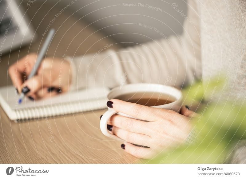 Frau hält eine Tasse Tee in der einen Hand und sie schreibt. Beteiligung schreibend arbeiten Schreibstift gemütlich trinken abschließen Kaukasier Pause