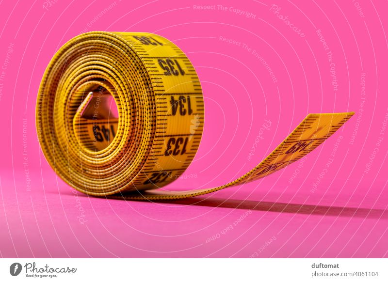 Makroaufnahme eines aufgerollten gelben Maßbandes auf pinkfarbenem Hintergrund Studioaufnahme Studiobeleuchtung rosa Rolle Meterband Band Rollup Diät abnehmen