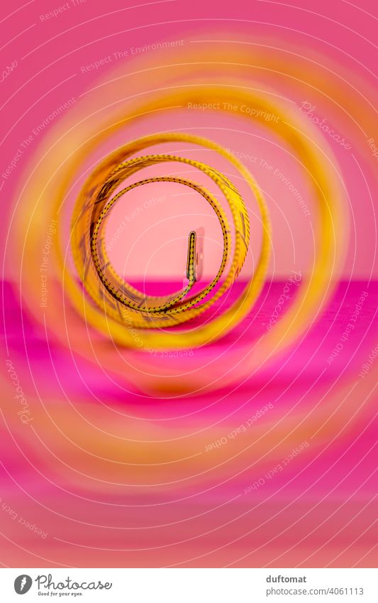 Makroaufnahme eines aufgerollten gelben Maßbandes auf Pinke Hintergrund Studioaufnahme Studiobeleuchtung rosa Rolle Meterband Band Rollup Diät abnehmen Frühling