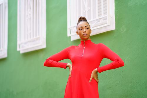 Junge schwarze Frau im roten Kleid vor einer grünen Wand Schleife ernst Frisur Behaarung Model Schönheit hübsch Porträt Mädchen jung Person Dame Sommer weiß