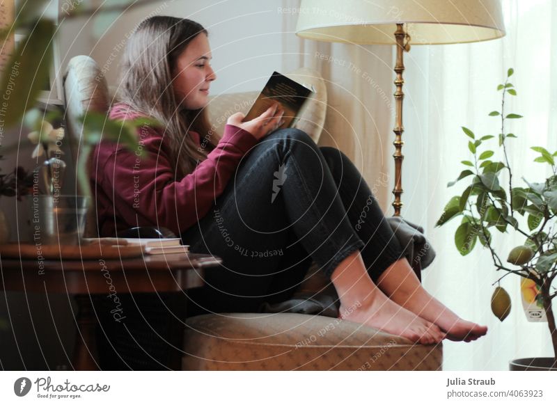 Teenager sitzt auf einem gemütlichen Ohrensessel und liest ein Buch Teenagermädchen teenager lesen Lesen eines Buches lesen bildet Barfuß barfüßig