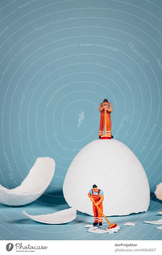 Reinigungskraft steht auf einem Ei während einen andere Figur die Schalen eines zebrochenen Eis zusammenfegt Miniatur minimalistisch fake künstlich Künstlerisch